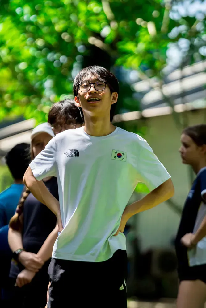 A young man wearing glasses and a white shirt is standing with his hands on his hips.
