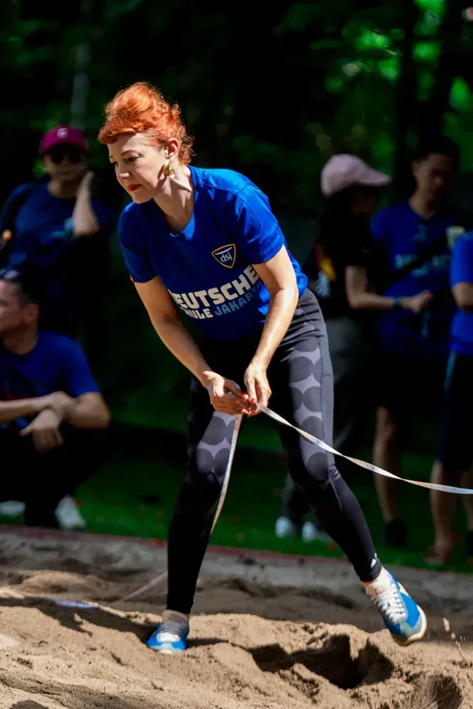 A woman in a blue shirt is jumping a rope in the sand.