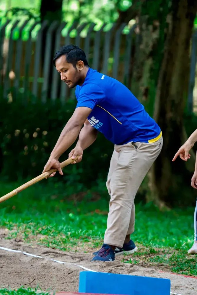 A man in a blue shirt is holding a wooden stick.