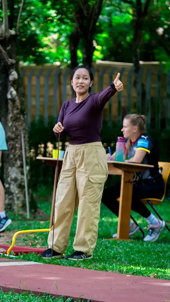 A woman is standing in the grass giving a thumbs up.
