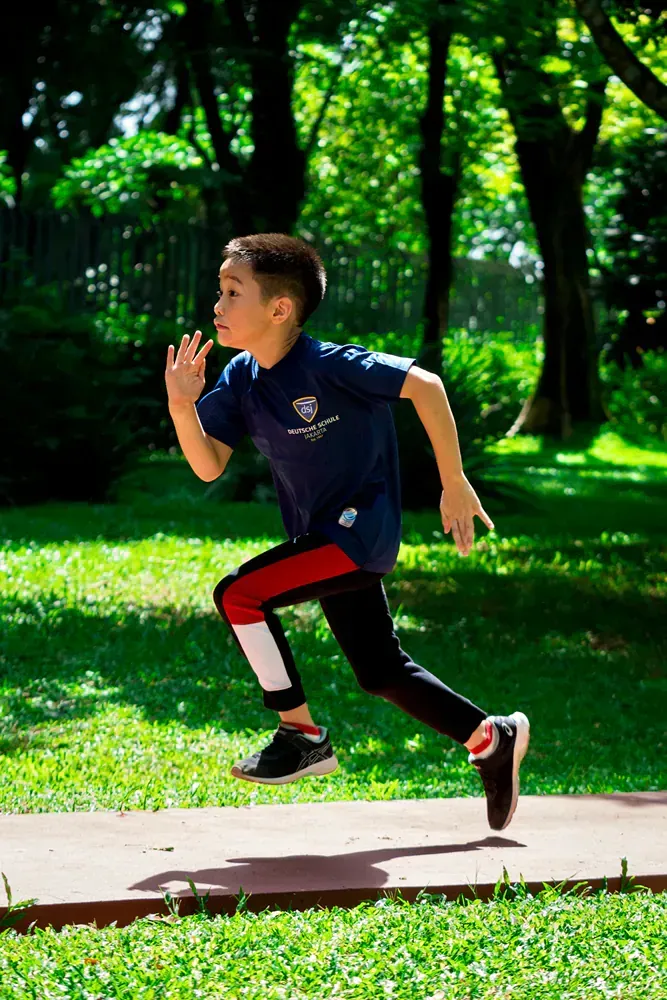 A young boy is running on a sidewalk in a park.