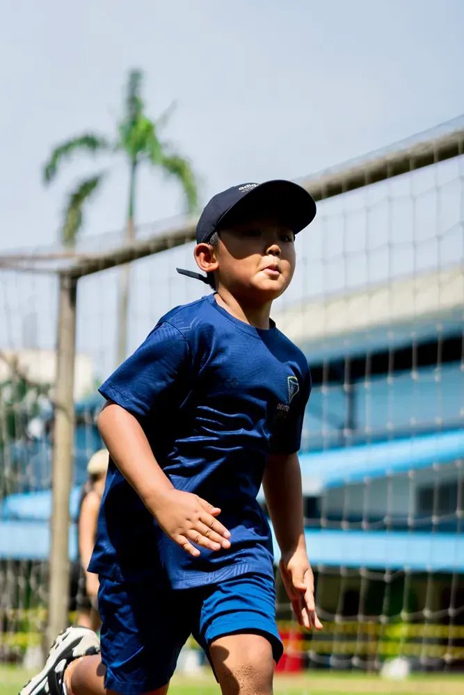A young boy in a blue shirt and shorts is running on a field.