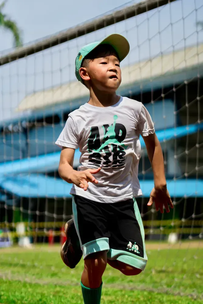 A young boy wearing a hat and shorts is running on a soccer field.