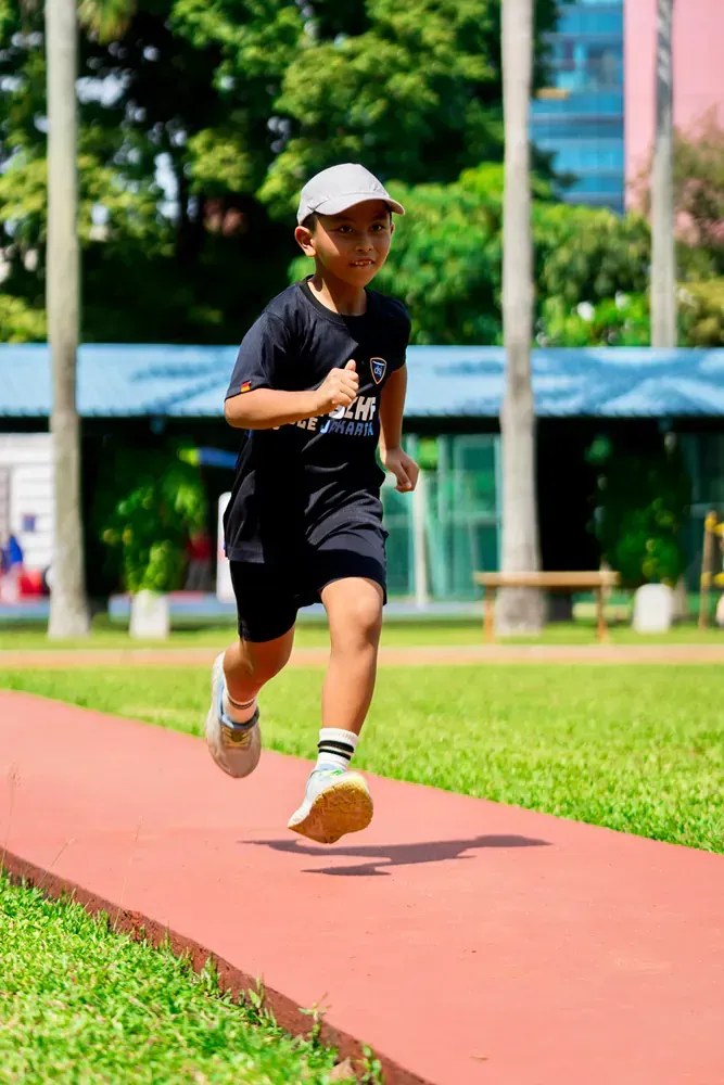 A young boy is running on a track in a park.
