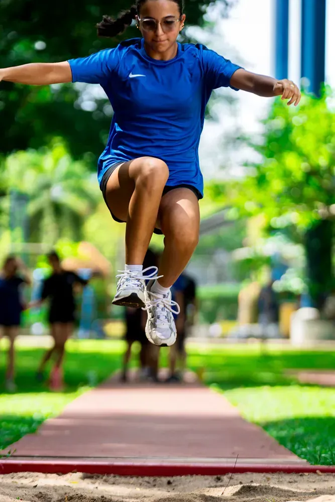 A woman in a blue shirt is jumping in the air on a track.