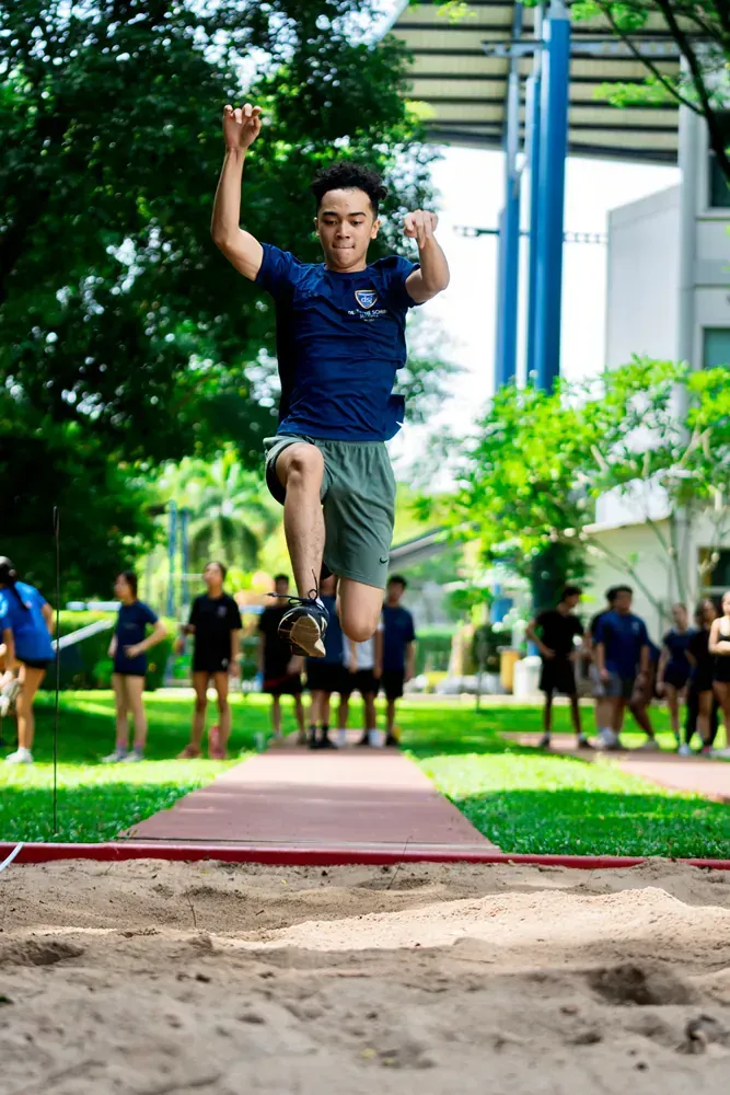 A young man is jumping in the air while competing in a long jump competition.