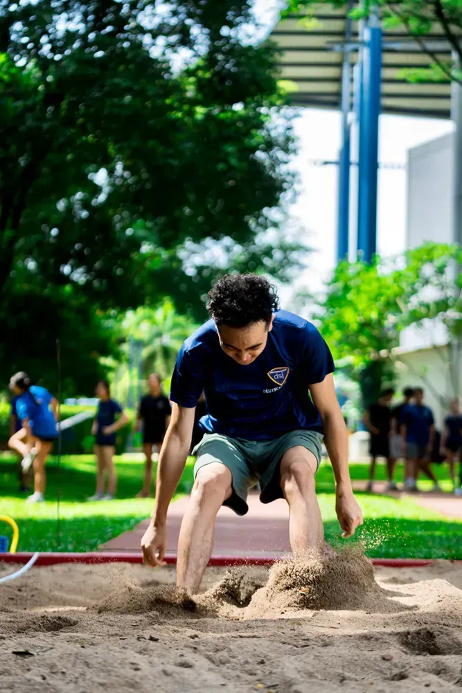 A man is jumping in the sand on a track.