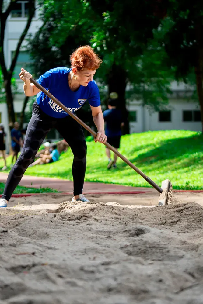 A woman is raking sand in a park with a rake.