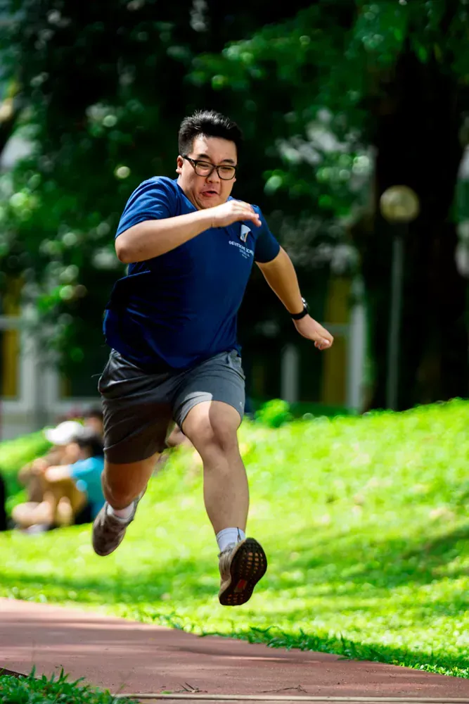 A man is jumping in the air while running on a track in a park.