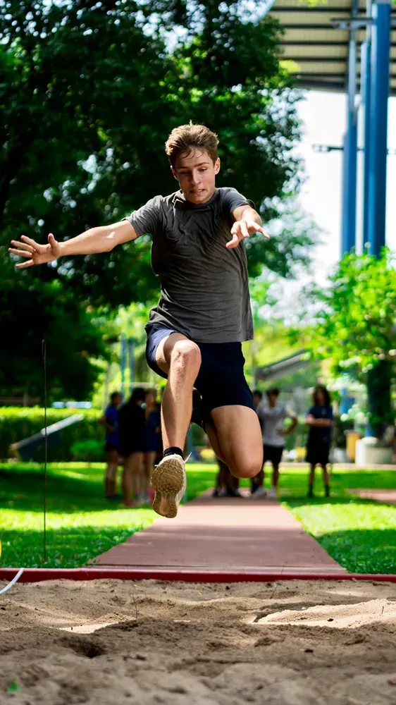 A young man is jumping in the air while doing a long jump.