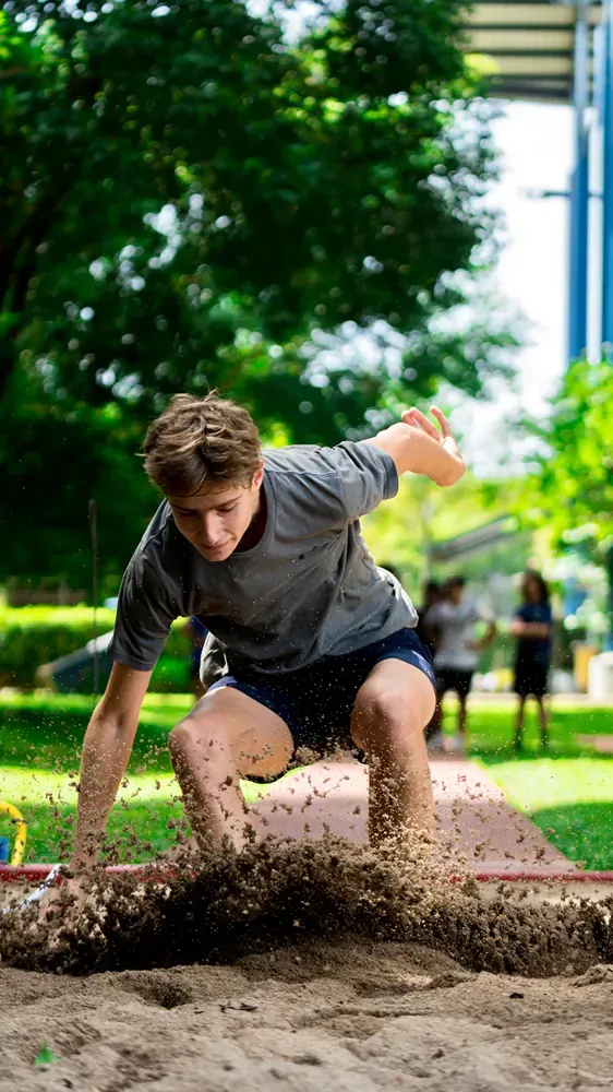 A young man is jumping a long jump in the dirt.