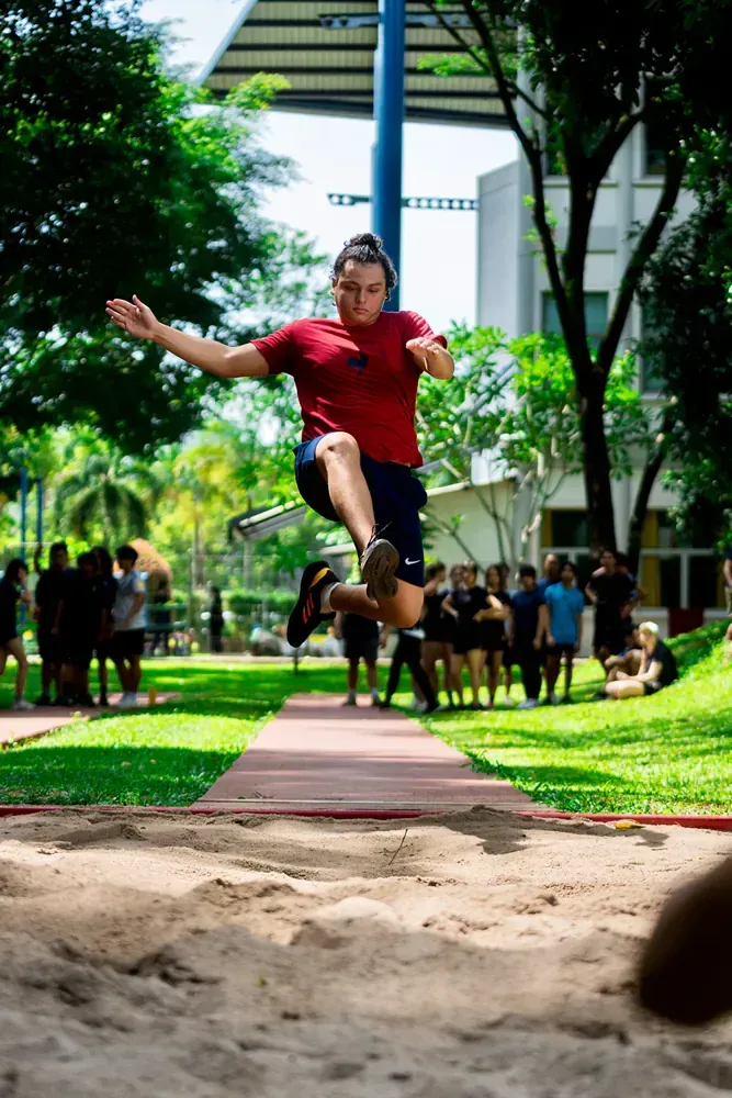 A man is jumping in the air while doing a long jump in a park.