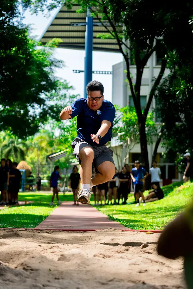 A man is jumping in the air while doing a long jump in a park.