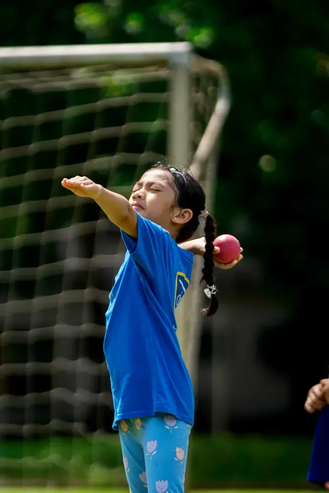 A young girl is throwing a ball in front of a soccer goal.