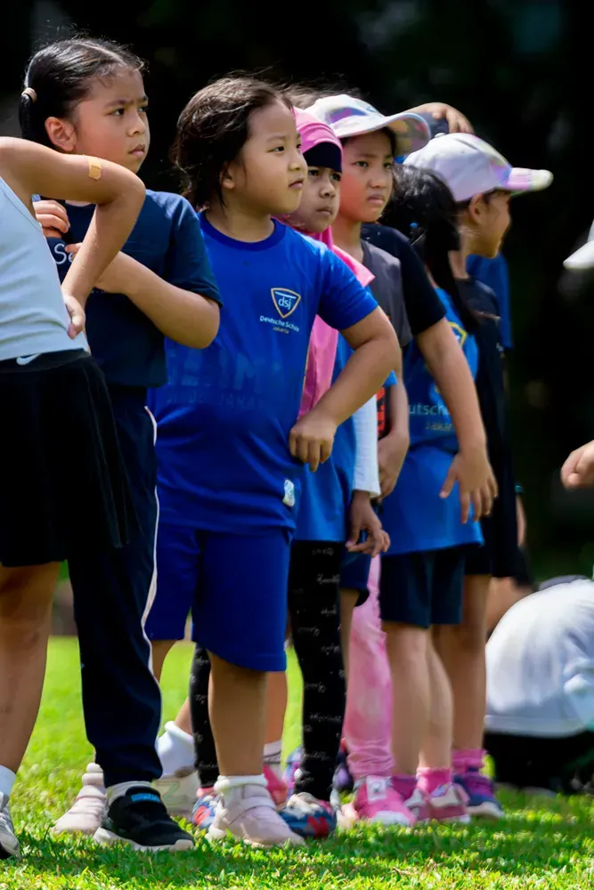 A group of young children are standing in a line on the grass.