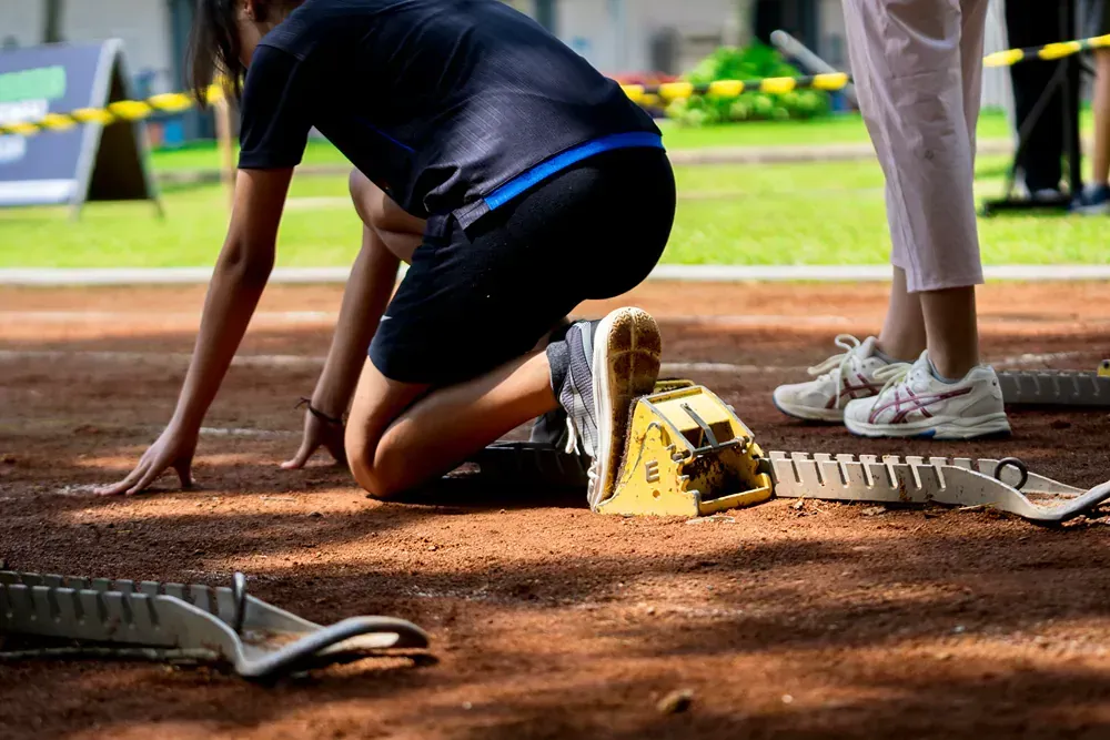 A person is kneeling down in front of a starting block on a track.
