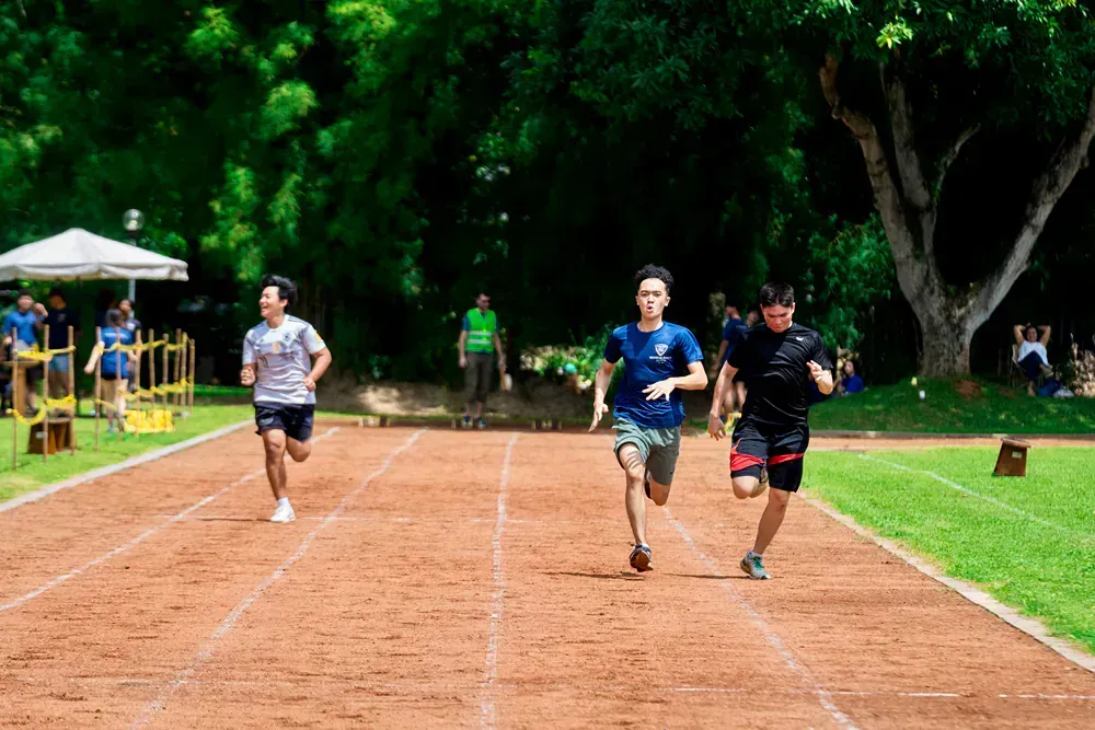 Three men are running on a track in a park.
