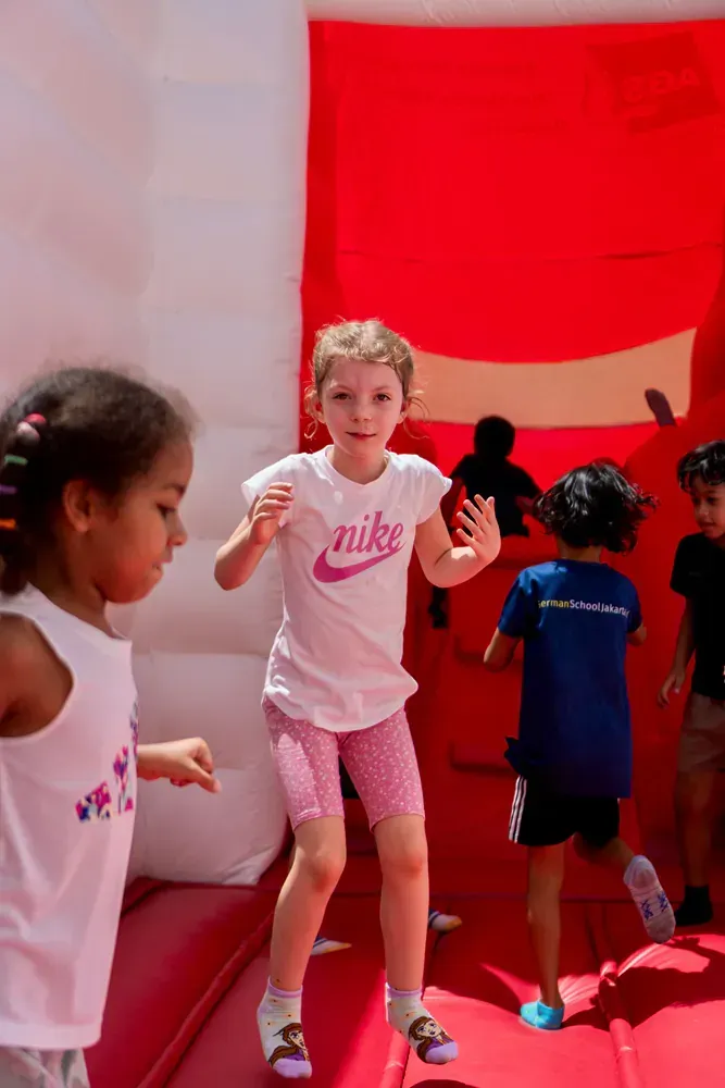A girl wearing a nike shirt is jumping on a bouncy house.