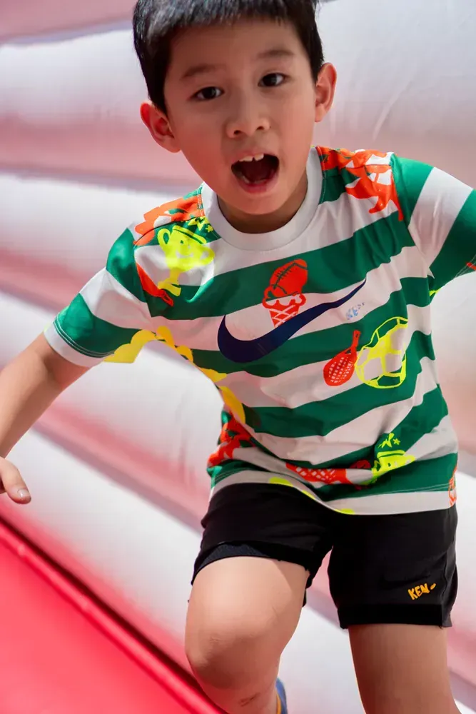 A young boy wearing a green and white striped shirt and black shorts is jumping on a bouncy house.