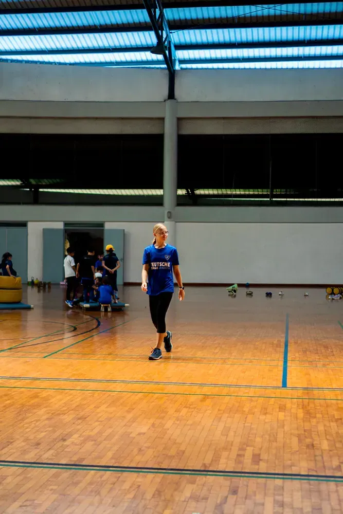 A man in a blue shirt is walking on a wooden floor in a gym.