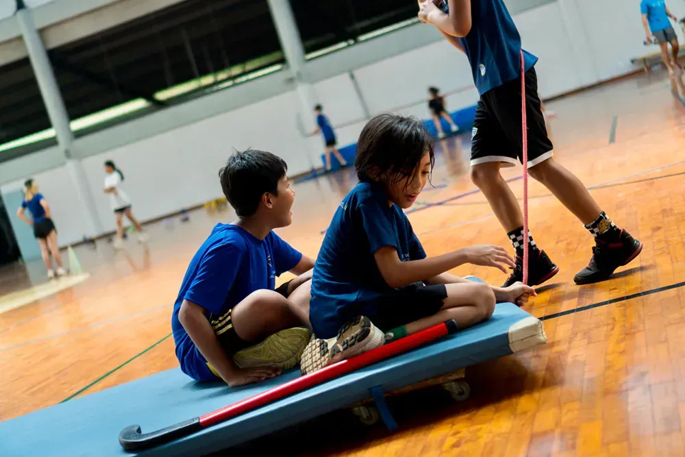 Two young boys are sitting on a blue mat in a gym.
