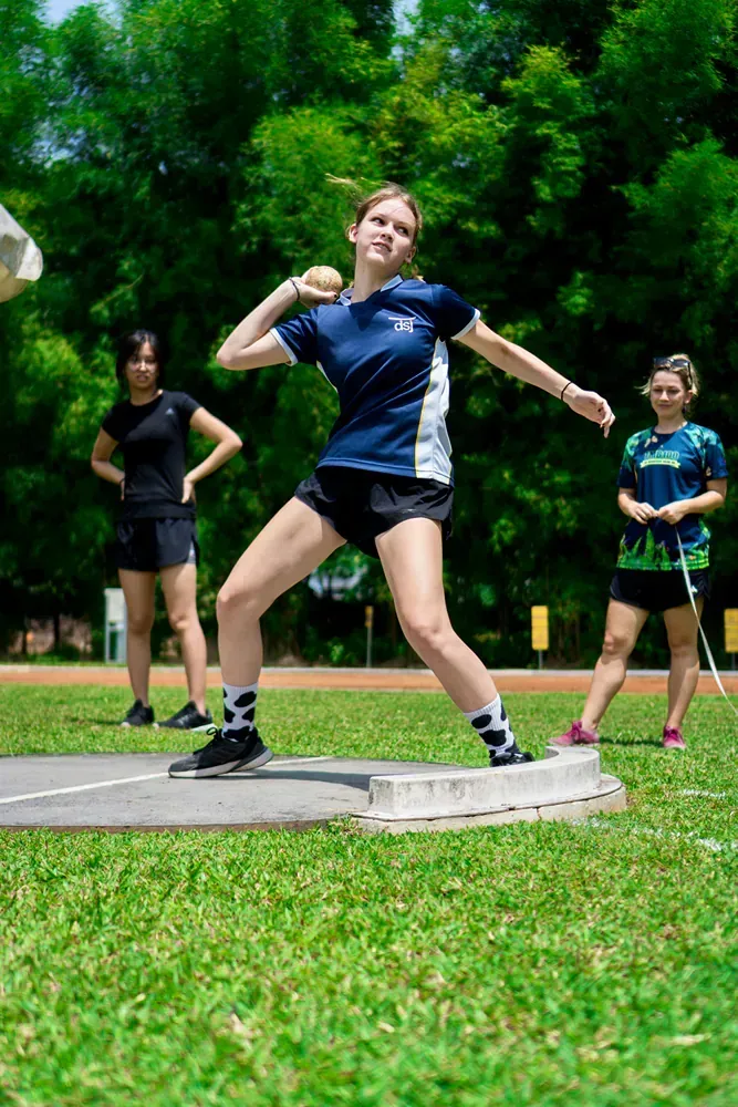 A woman is throwing a shot put in a field.