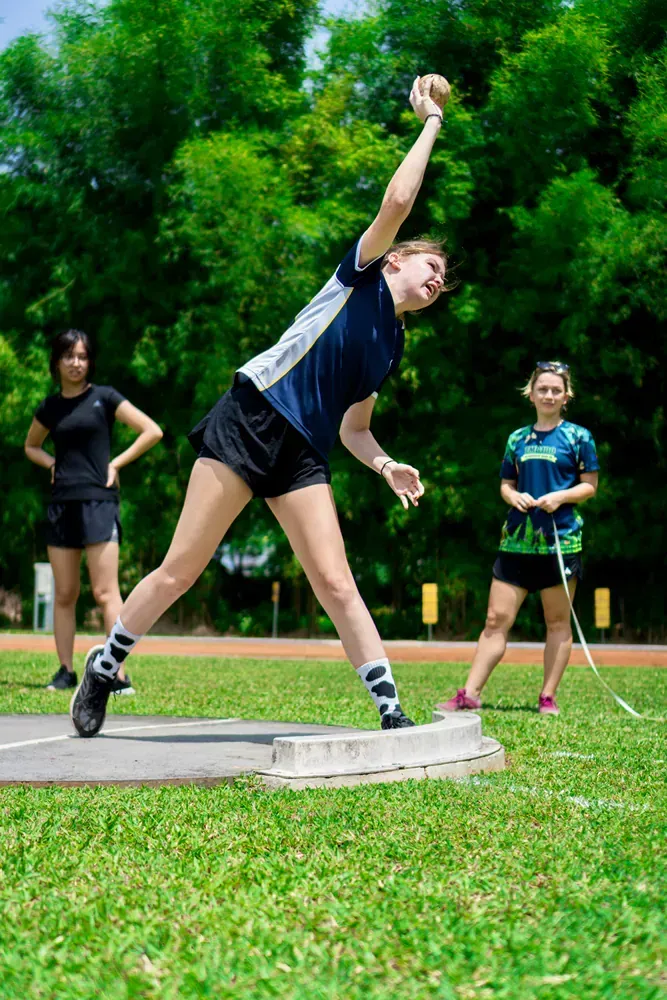 A woman is throwing a shot put in a field.