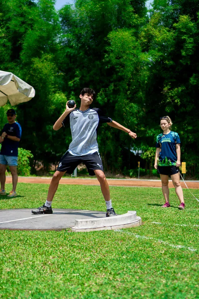 A young man is throwing a shot put ball in a field.