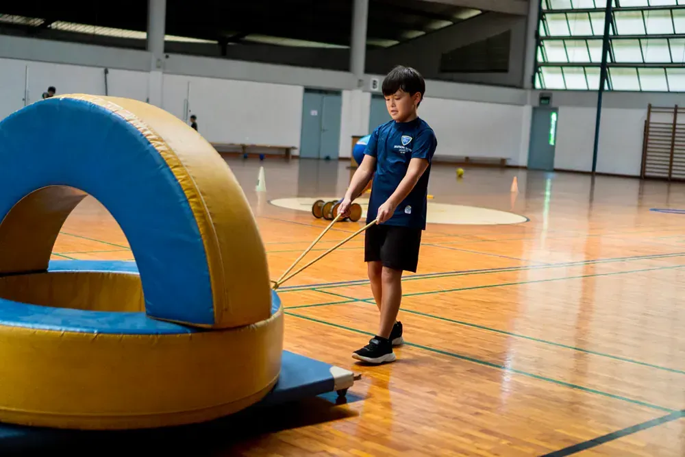 A young boy is pulling a large inflatable object with a rope in a gym.