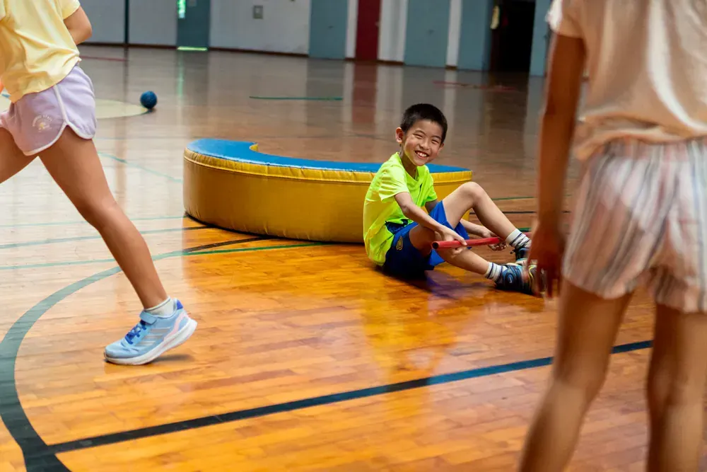 A boy is sitting on the floor of a gym holding a ball.