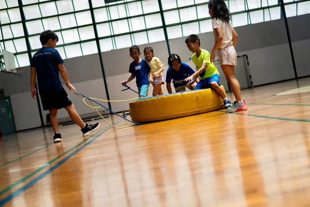 A group of children are playing with a tire in a gym.