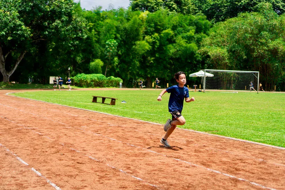 A young boy is running on a track in a park.