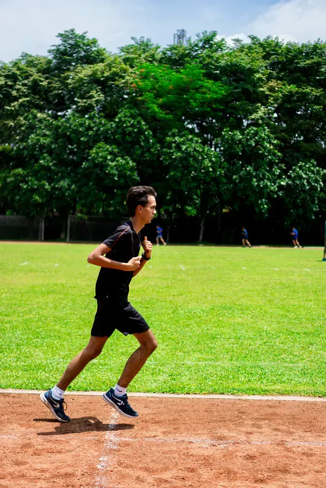 A young man is running on a track in a park.