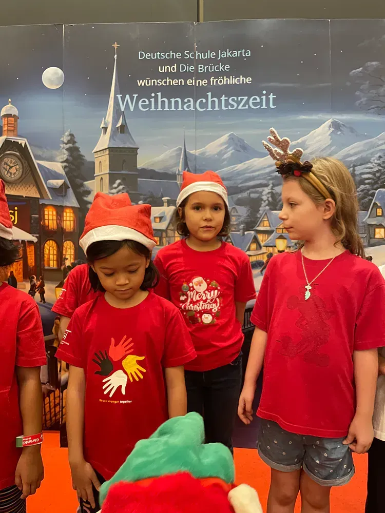 A group of children wearing red shirts and santa hats are standing next to each other.