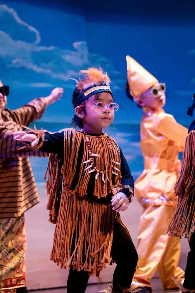 A group of children dressed in native american costumes are dancing on a stage.