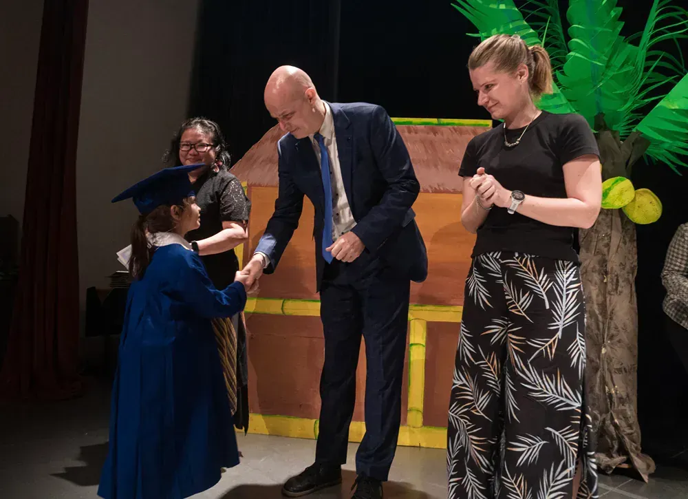 A little girl in a graduation cap and gown is shaking hands with a man in a suit and tie.