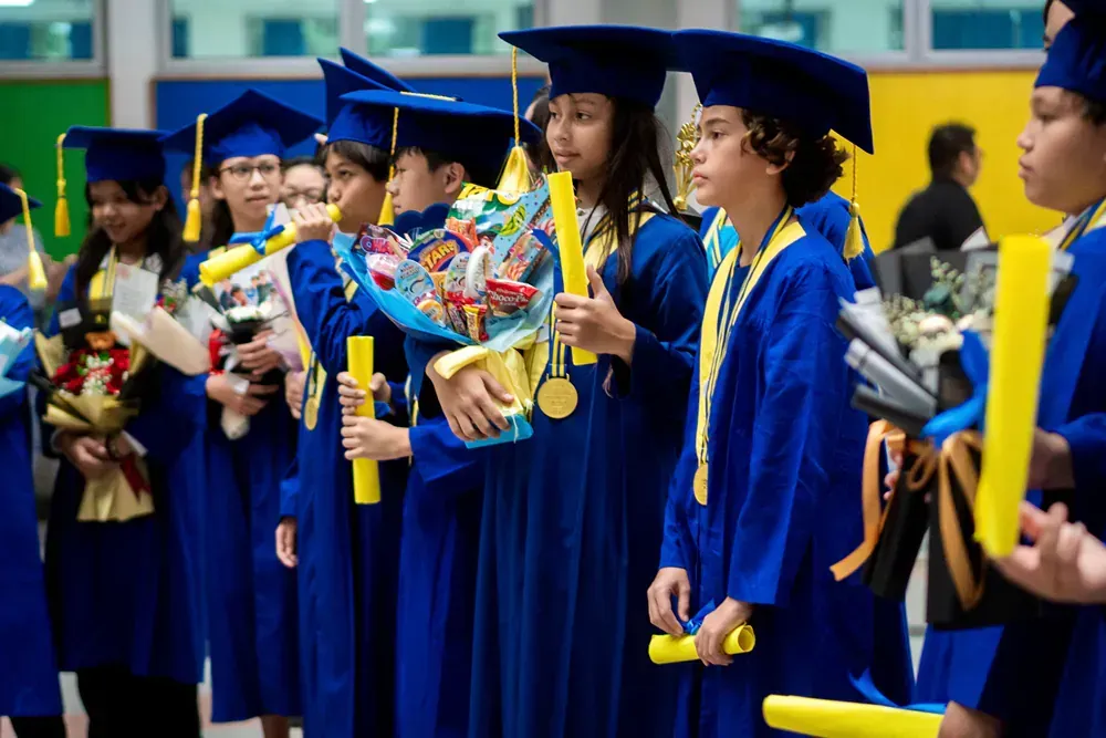 A group of young graduates are standing in a line holding diplomas and flowers.