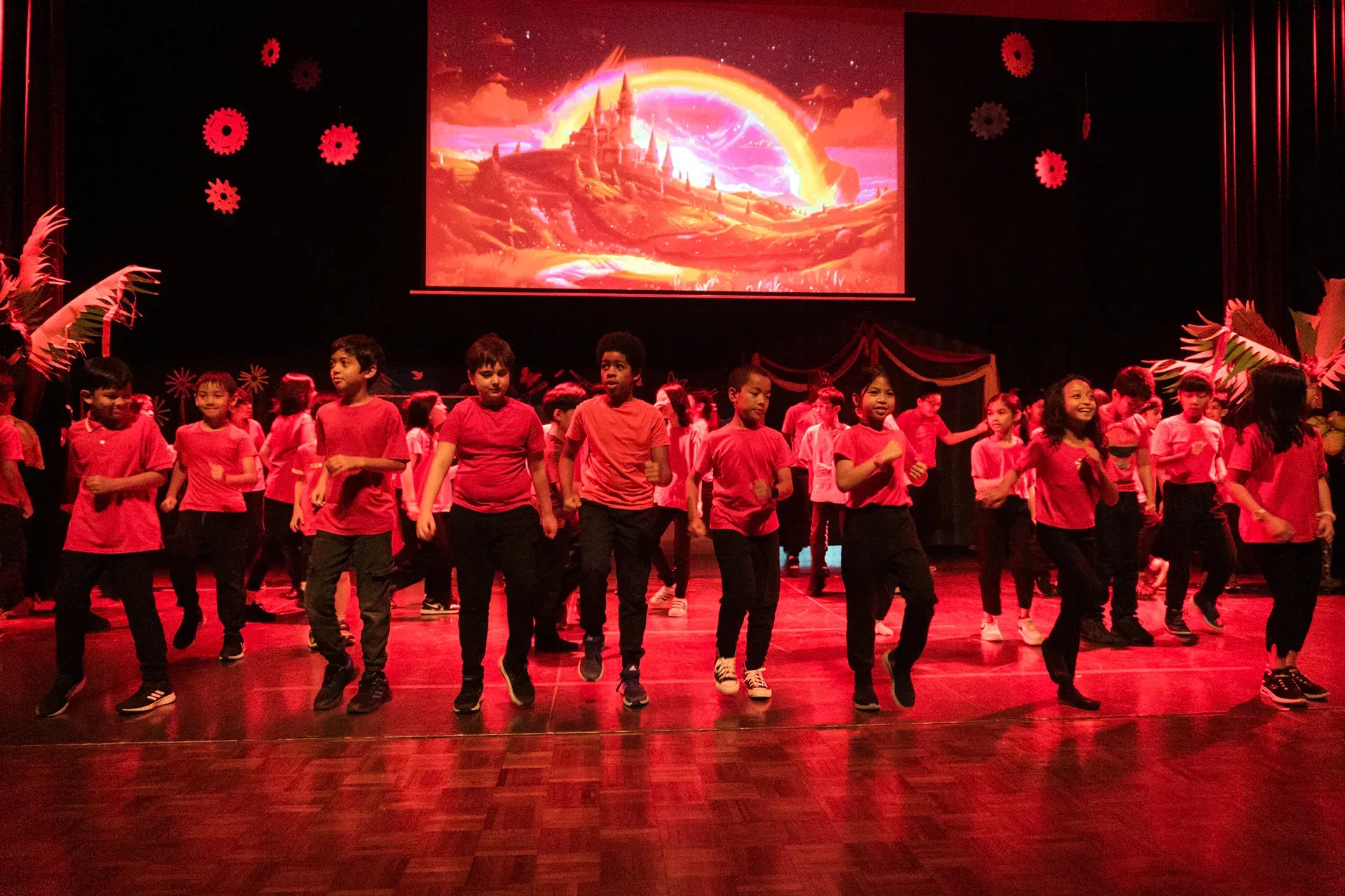 A group of children are dancing on a stage in front of a large screen.