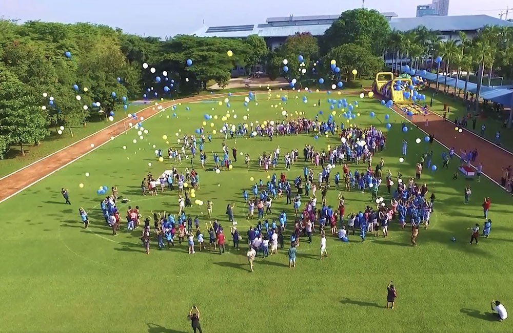 A large group of people are standing in a field with balloons flying in the air.