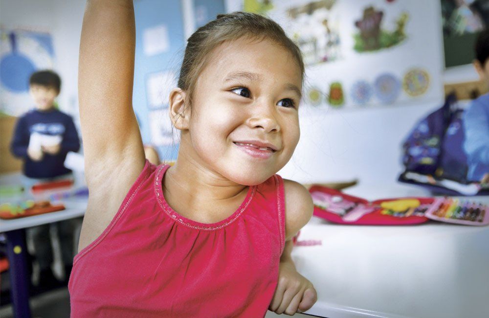 A little girl is raising her hand in a classroom.