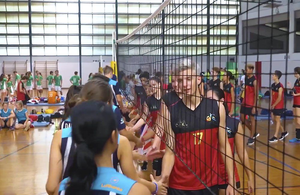 A group of people are standing around a volleyball net in a gym.