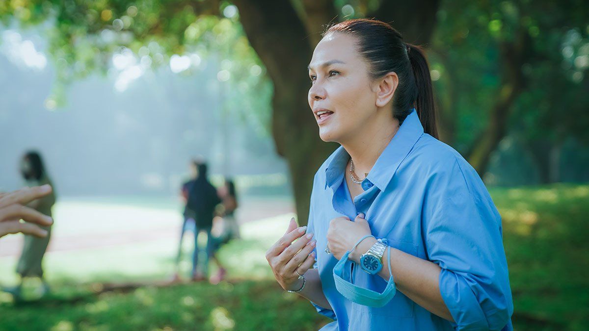 A woman in a blue shirt is standing in a park.