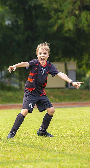 A young boy is standing on a soccer field with his arms outstretched.