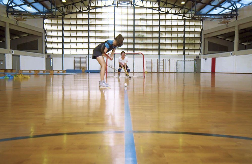 A man and a woman are playing a game of floorball in a gym.