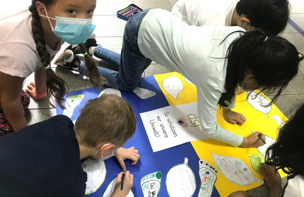 A group of children are sitting on the floor drawing on a large piece of paper.