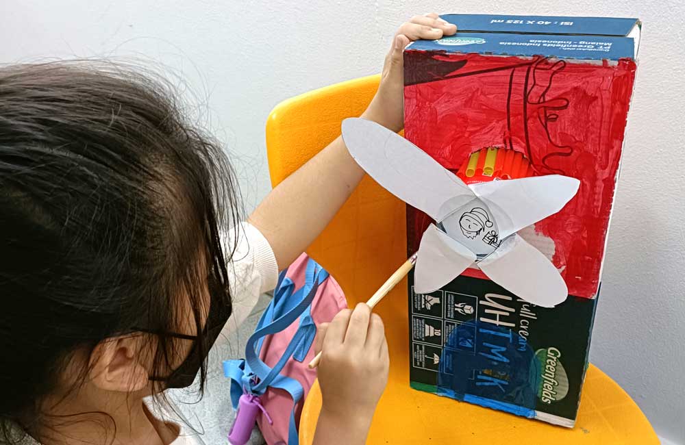 A little girl is making a paper airplane out of a cardboard box.