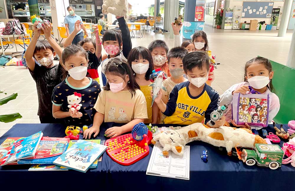 A group of school children wearing face masks are sitting around a table with toys.