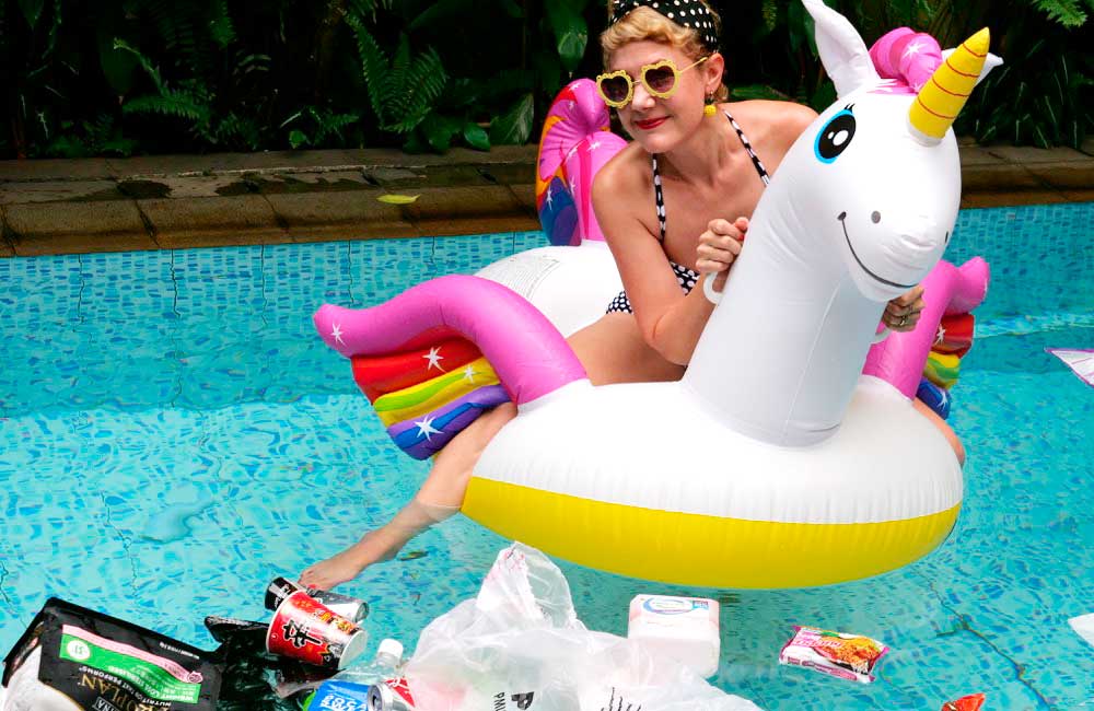 A woman is sitting on an inflatable unicorn in a swimming pool.