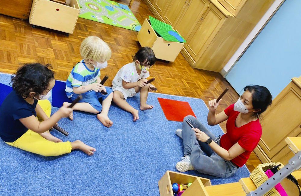 A woman wearing a mask is sitting on the floor with three children.