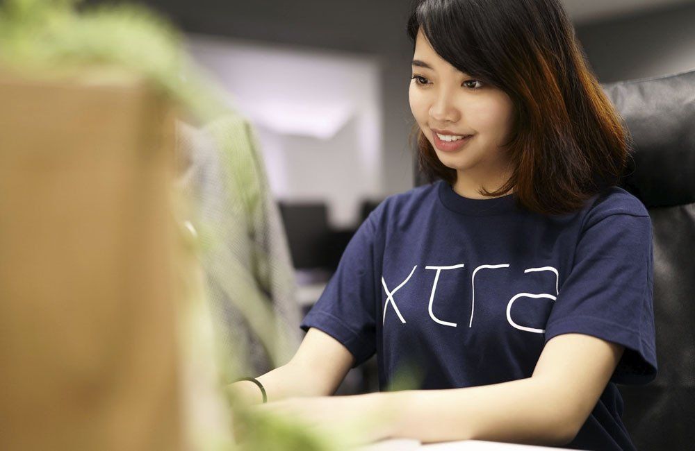 A woman in a blue shirt is sitting at a desk in front of a computer.